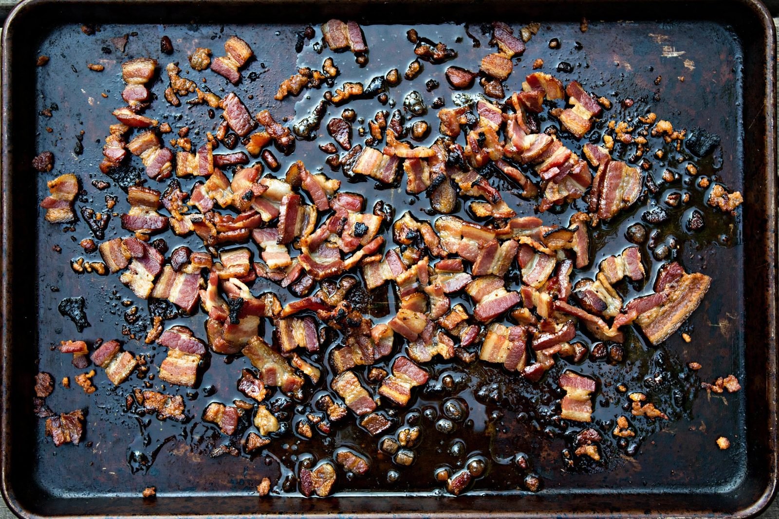 Partially crisped chopped bacon spread on a sheet pan with rendered bacon fat.