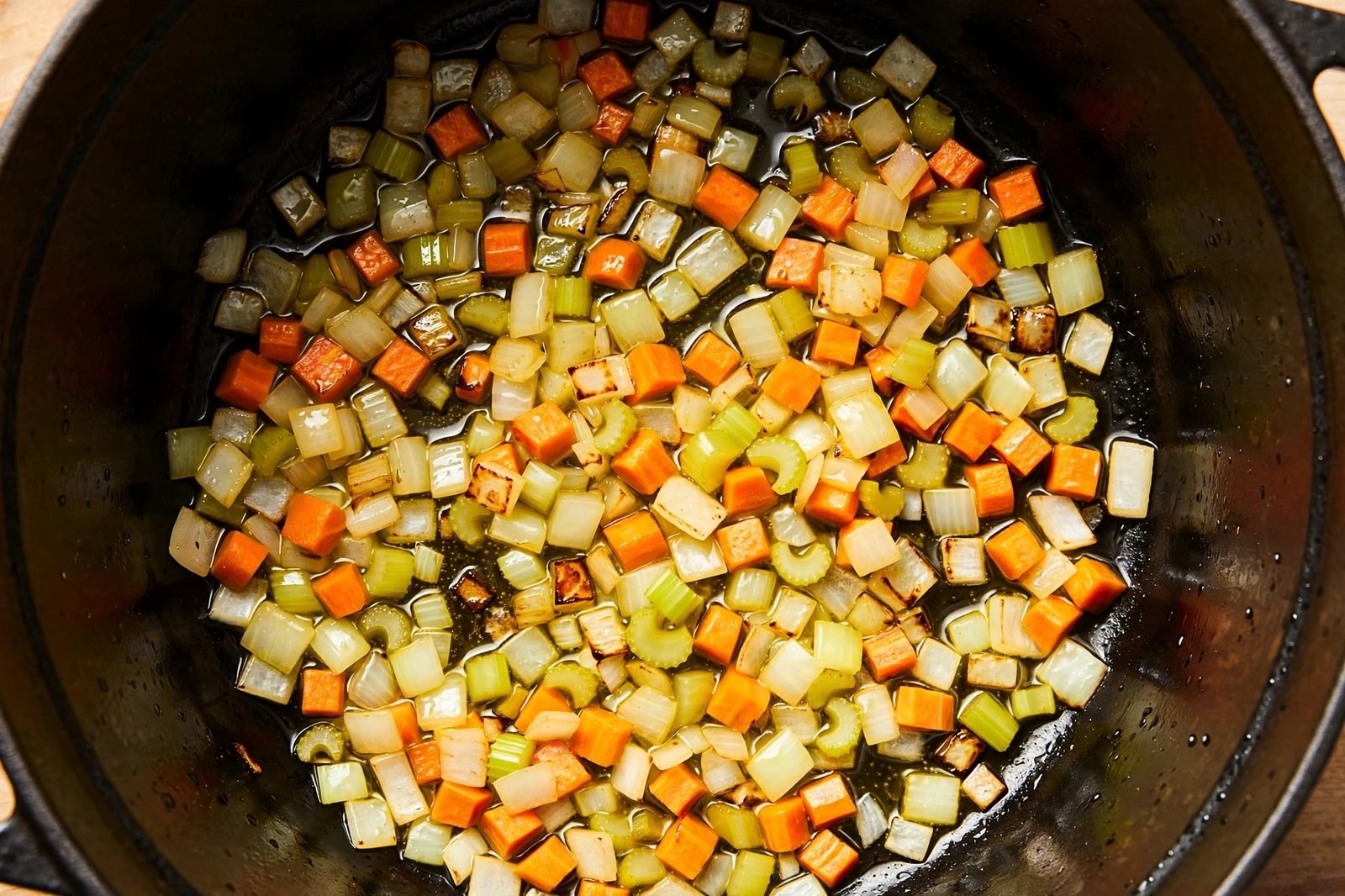 Diced onion, carrots, and celery sautéing in olive oil in a Dutch oven.
