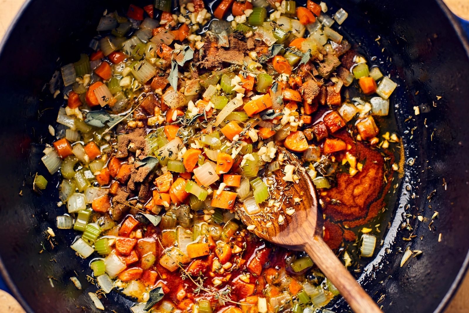 Minced garlic, sage, thyme, and paprika being stirred into softened vegetables.