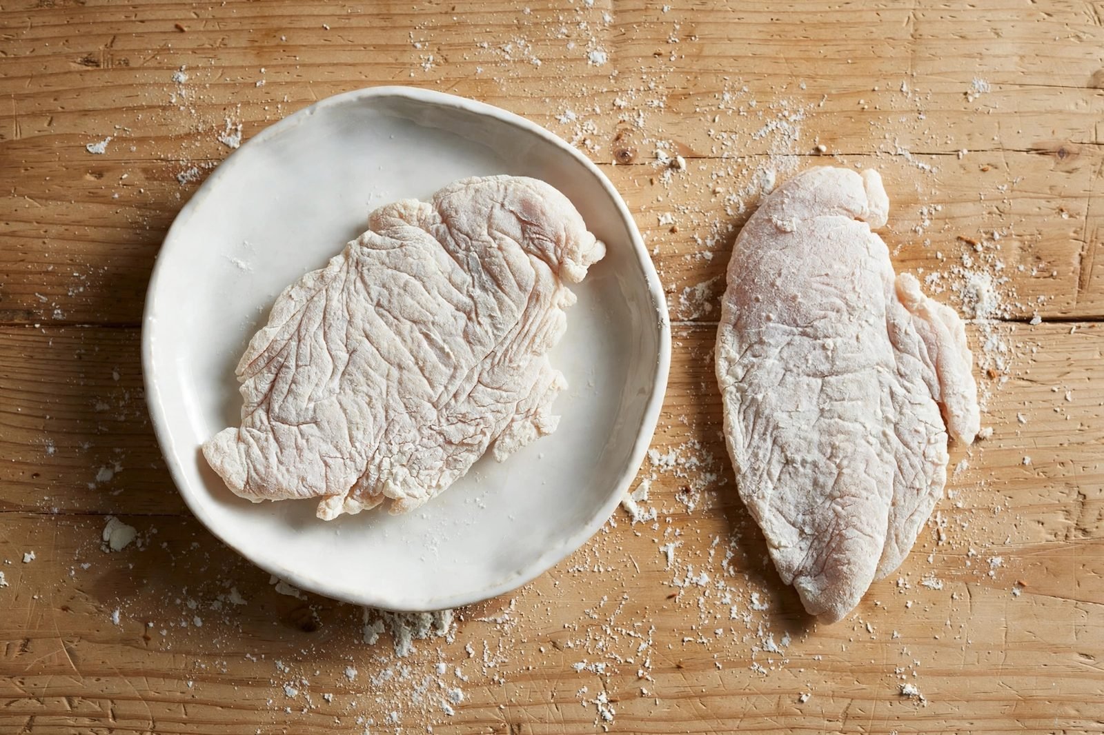 Overhead of chicken cutlets dredged in flour in a shallow dish, excess shaken off.