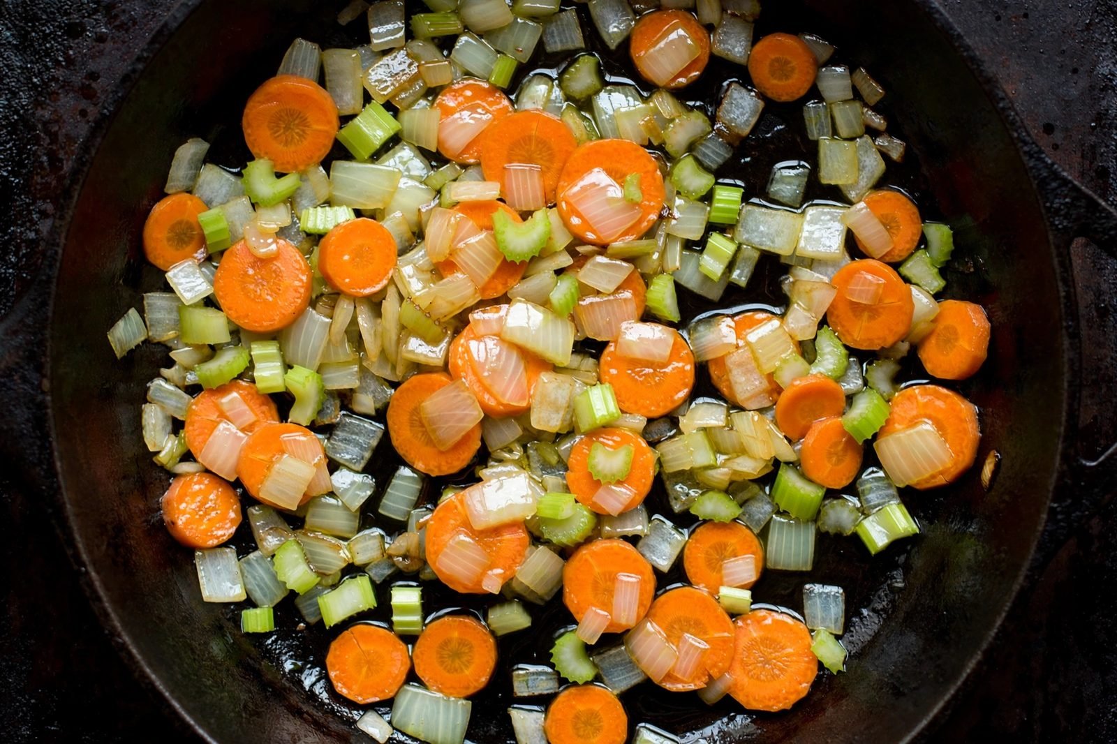 Overhead of diced onion, carrots, and celery softening in the skillet.