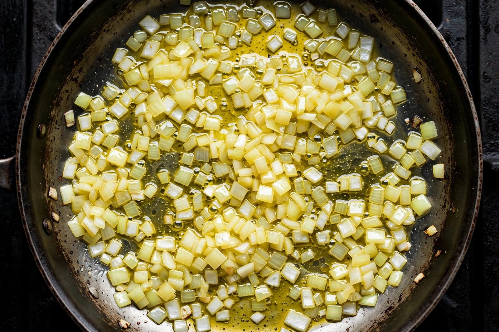 Overhead of diced onion softening in the skillet with olive oil. No people, no text.