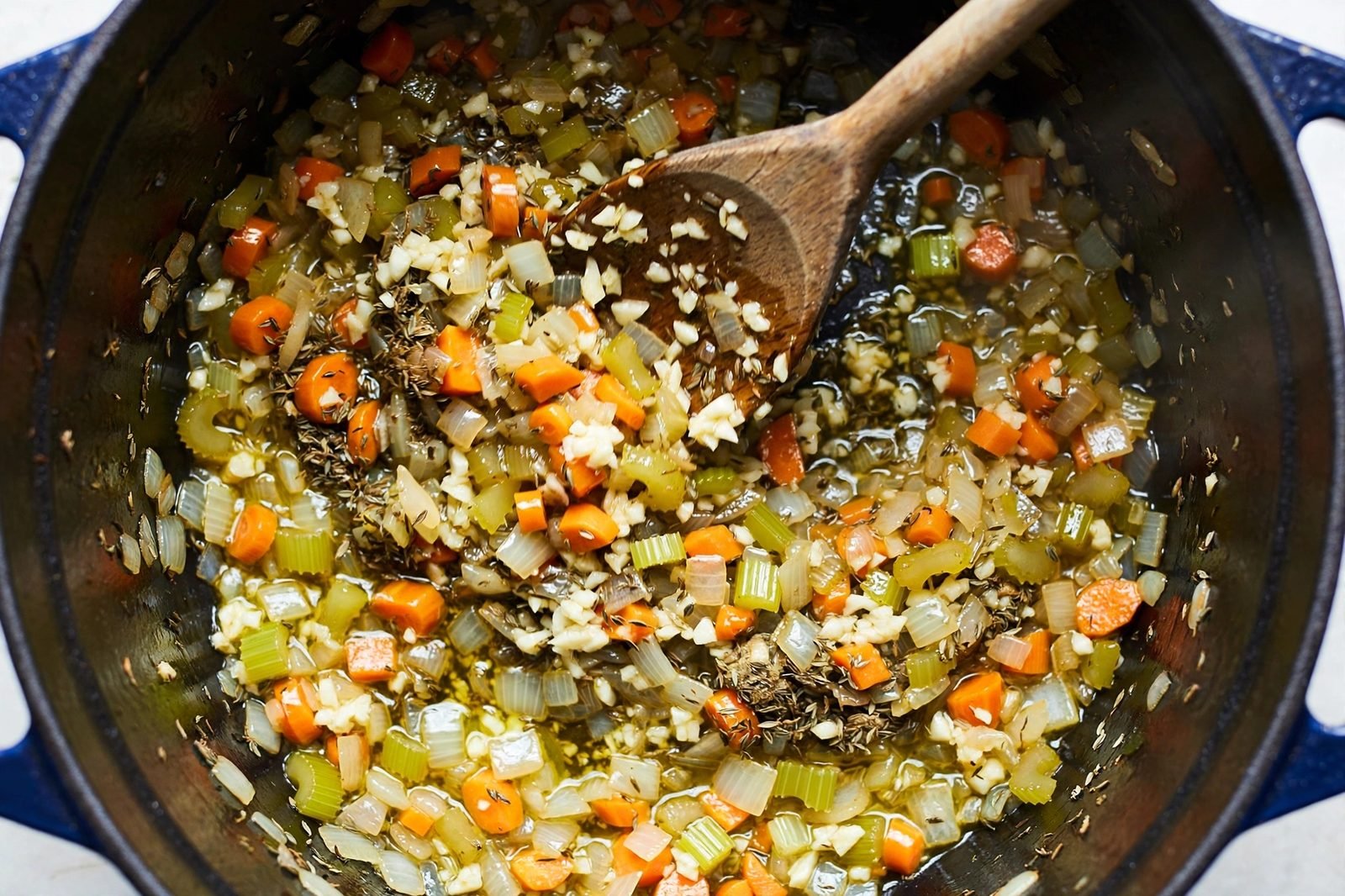 Overhead of minced garlic and thyme being stirred into the vegetables. No people, no text.
