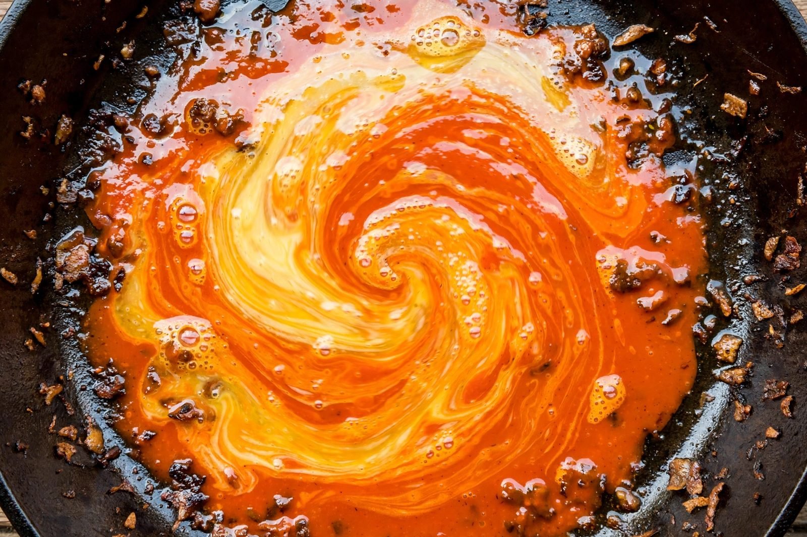 Overhead of butter and buffalo hot sauce melting into a glossy sauce in the skillet. No people, no text.