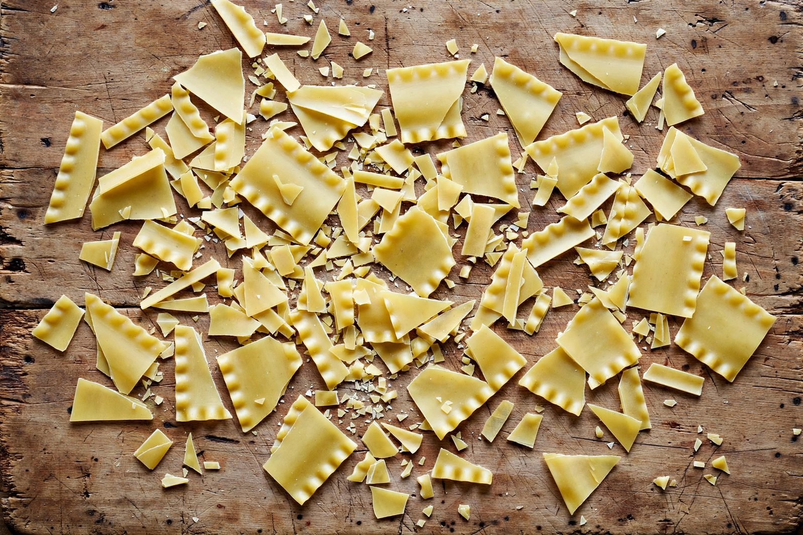 Overhead of lasagna sheets broken into pieces on a cutting board. No people, no text.